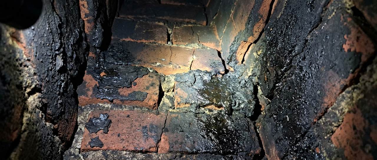 Close-up of heavy dark creosote deposits coating the interior of a masonry chimney flue